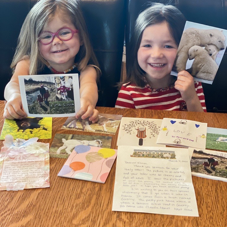 Two adorable girls reading letters from those they care about spread out on a table before them.